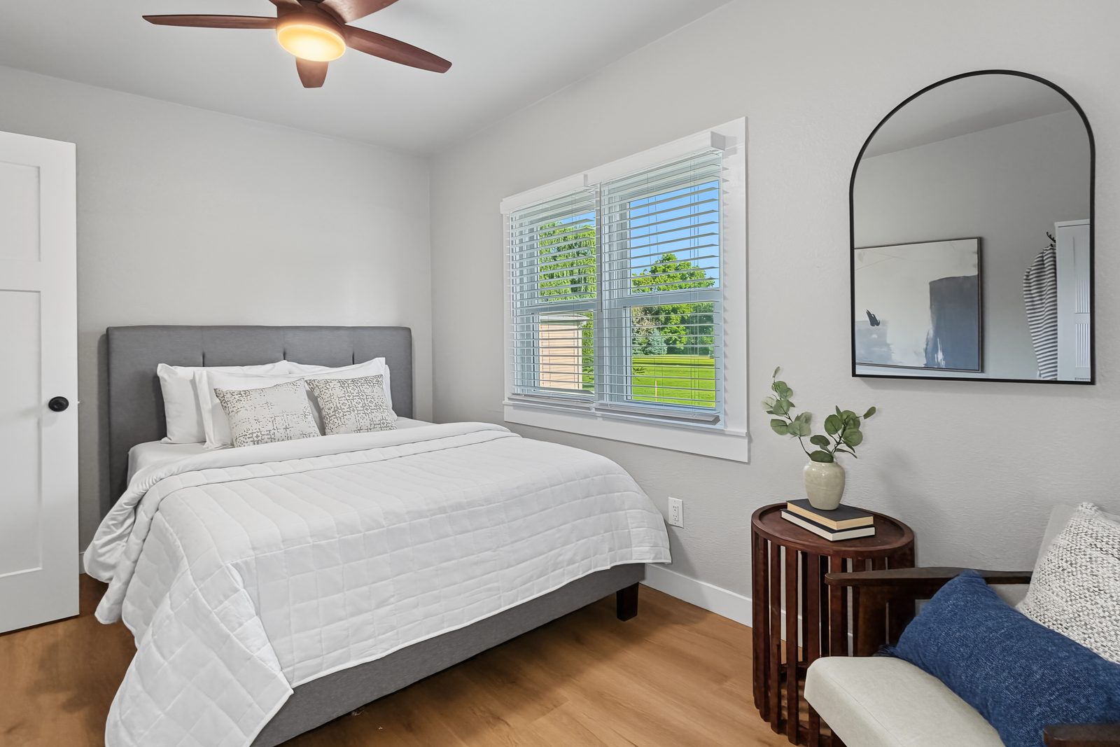 Second bedroom with upholstered bed, arched mirror, and corner window at 3436 Scott Ave Des Moines Iowa